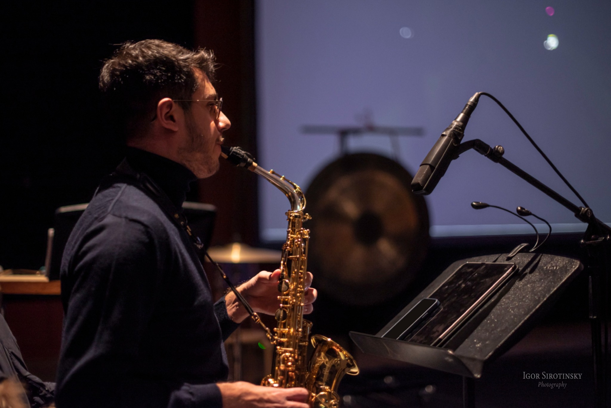 Close-up of Alberto Cavallaro playing saxophone beside a microphone and music stand.